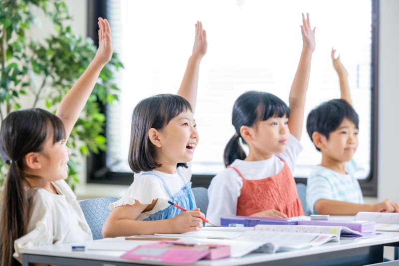 授業で元気よく手を上げる小学生たち