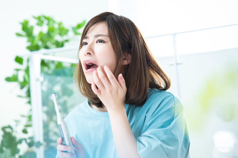 銀歯の下の虫歯が気になって鏡でチェックする女性